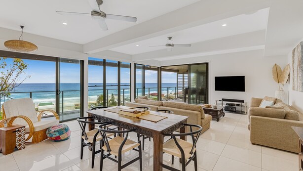 A spacious living area with a large window overlooking the ocean, a dining table with chairs, and a sofa.
