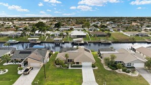 A residential area with houses, a canal, and a dock with boats. - Gulf access villa w/saltwater heated pool & boat lift! Villa Delieta - SWFL Rentals (Cape Coral)