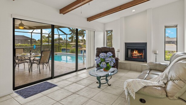 A spacious living room with a fireplace, a pool view, and a comfortable seating area. - Gulf access villa w/saltwater heated pool & boat lift! Villa Delieta - SWFL Rentals (Cape Coral)