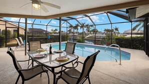 A poolside area with a glass table and chairs, a ceiling fan, and a view of the pool and surrounding neighborhood. - Gulf access villa w/saltwater heated pool & boat lift! Villa Delieta - SWFL Rentals (Cape Coral)