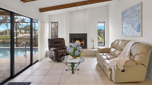 A spacious living room with a fireplace, a pool view, and a beige sofa. - Gulf access villa w/saltwater heated pool & boat lift! Villa Delieta - SWFL Rentals (Cape Coral)