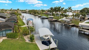 A canal with boats docked, surrounded by residential houses and palm trees. - Gulf access villa w/saltwater heated pool & boat lift! Villa Delieta - SWFL Rentals (Cape Coral)