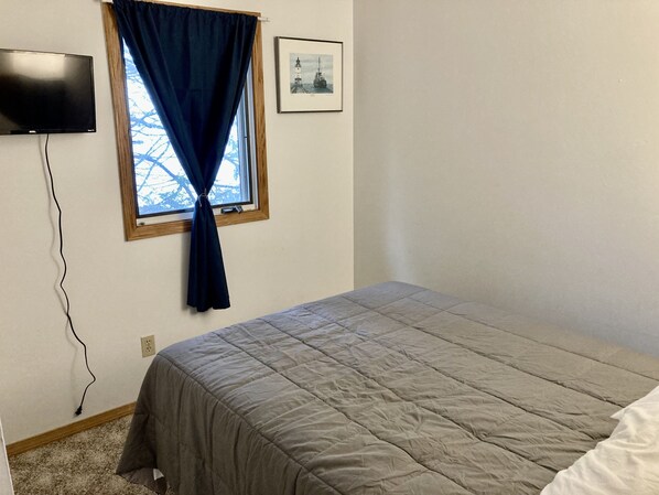 A bedroom with a bed, a TV, a window with curtains, and a framed picture on the wall. - Lake Superior View ~ Convenient ~ In town (Munising)