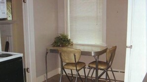 Un petit coin repas avec une table et quatre chaises, une fenêtre avec des stores et une plante posée sur la table.