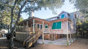 A two-story wooden cabin with a deck, a covered porch, and a fenced yard. -  Serene Sanderling Beach Cottage Steps from beach w/community pool - Duck  (Duck)