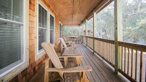 A wooden deck with Adirondack chairs and a table, surrounded by wooden walls and large windows. -  Serene Sanderling Beach Cottage Steps from beach w/community pool - Duck  (Duck)