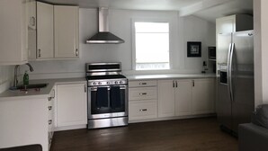 A modern kitchen with white cabinets, stainless steel appliances, a window, and a grey sofa. - Fay Cottage - Convenience in the heart of La Jolla village of La Jolla (La Jolla)
