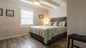 A bedroom with a bed, a window, a ceiling fan, and framed pictures on the wall. - Coastal charmer in the Heart of Port Aransas (Port Aransas)