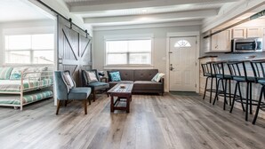A spacious living area with a sofa, chairs, a coffee table, and a kitchen with a microwave and bar stools. - Coastal charmer in the Heart of Port Aransas (Port Aransas)