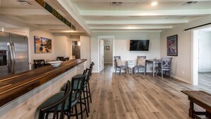 A spacious kitchen with a wooden bar counter, a refrigerator, and a dining area with a table and chairs. - Coastal charmer in the Heart of Port Aransas (Port Aransas)