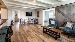 A spacious living room with a wooden floor, a large wooden door, and a television mounted on the wall. - Coastal charmer in the Heart of Port Aransas (Port Aransas)