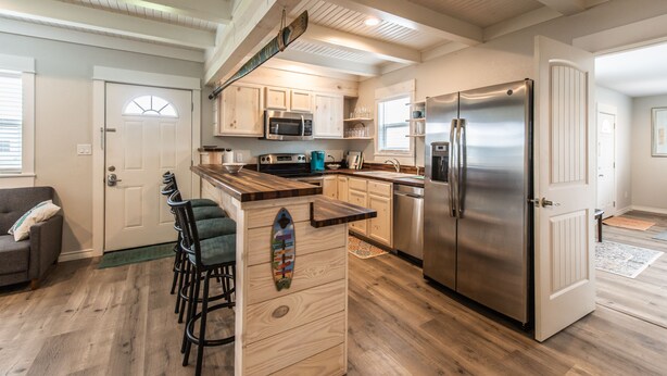 A modern kitchen with wooden cabinets, a stainless steel refrigerator, and a bar area with stools. - Coastal charmer in the Heart of Port Aransas (Port Aransas)