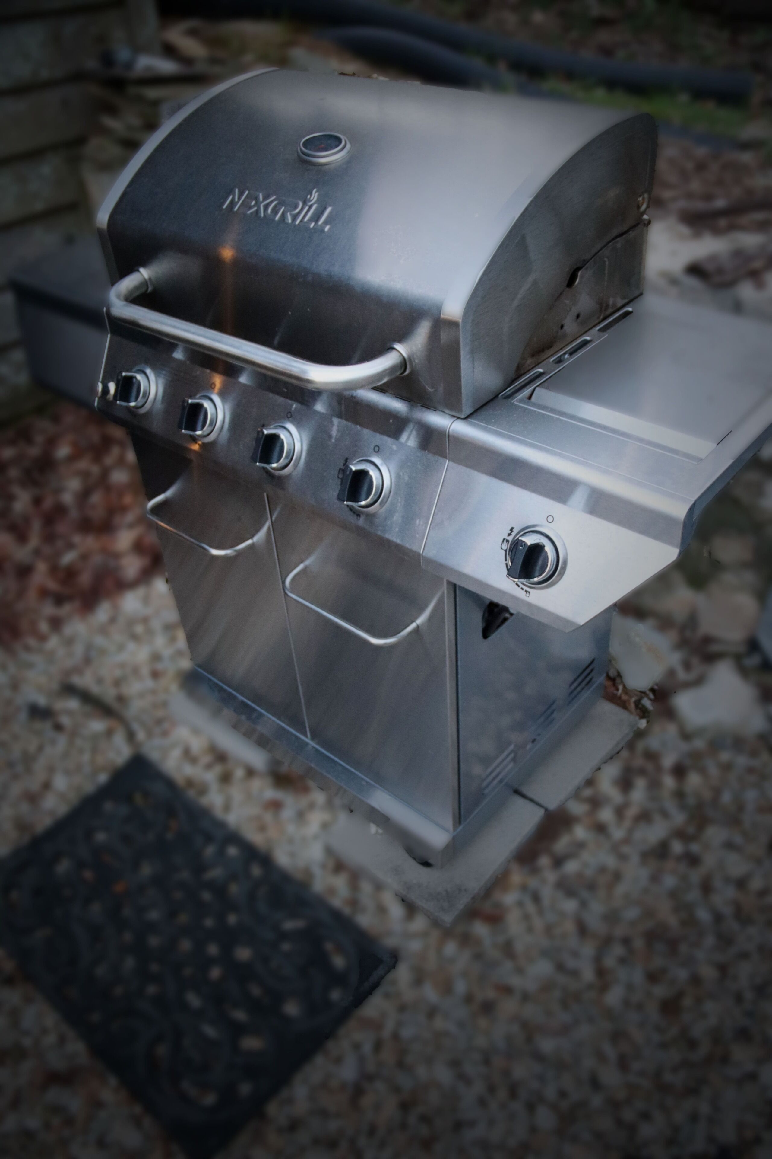 Un barbecue NEXGRILL en acier inoxydable, doté de quatre brûleurs et d’une étagère latérale.