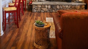 A living room with a stone fireplace, red chairs, a wicker side table, and a leather sofa.
