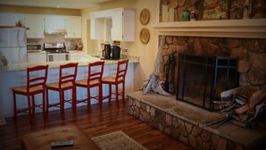A spacious living area with a stone fireplace, a kitchen with white cabinets, and a dining area with red chairs.