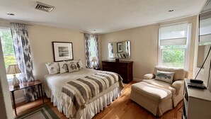 A bedroom with a bed, a bedside table, a dresser, a chair, and a window.