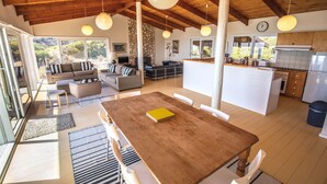 A spacious living area with a wooden dining table, sofas, and a kitchen with a stone wall and wooden beams. - King George Beach Retreat (Middle River)