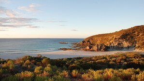A coastal landscape with a beach, rocky cliffs, and dense shrubbery. - King George Beach Retreat (Middle River)