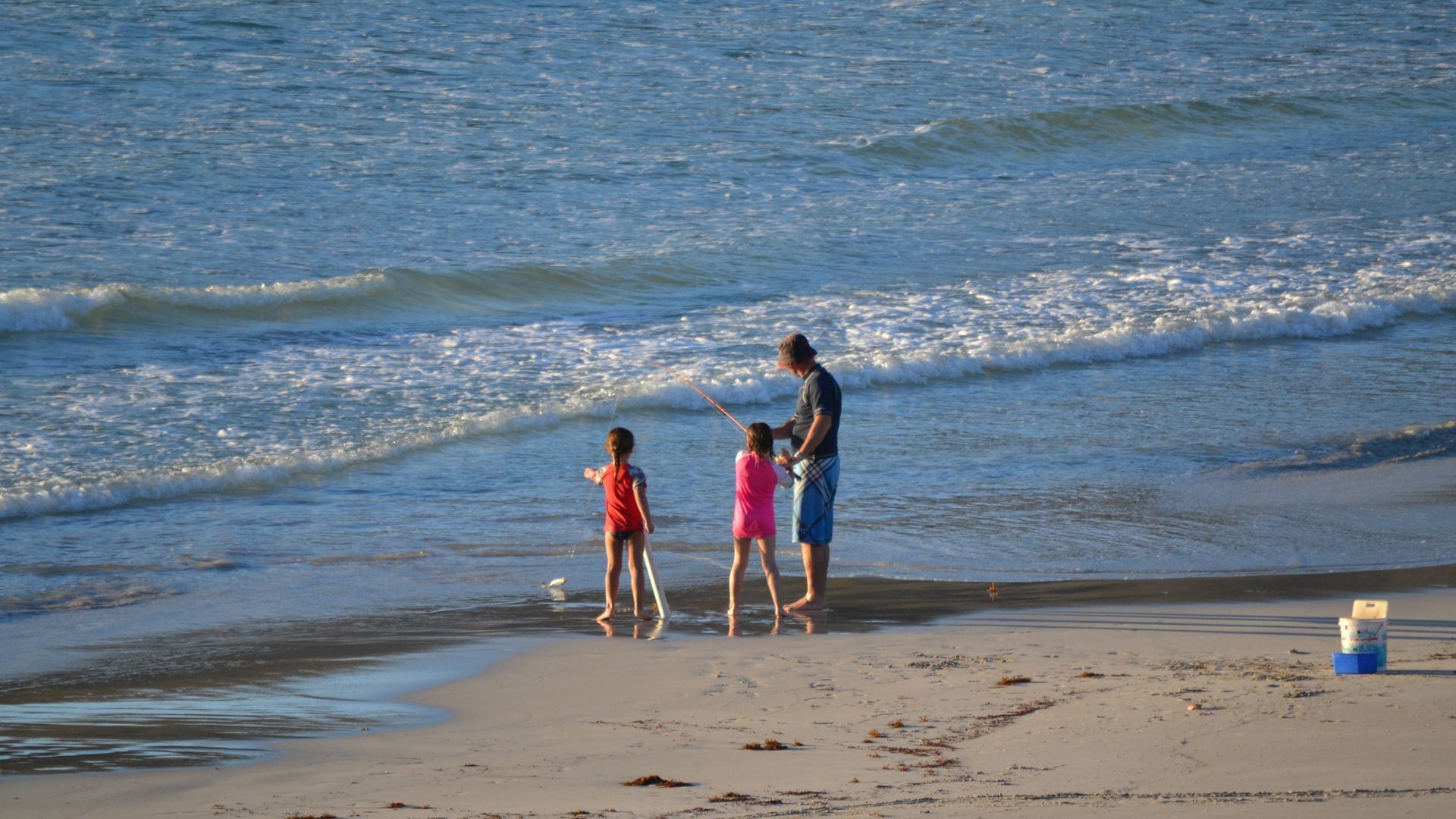 A beach scene with a family of three and a man fishing.