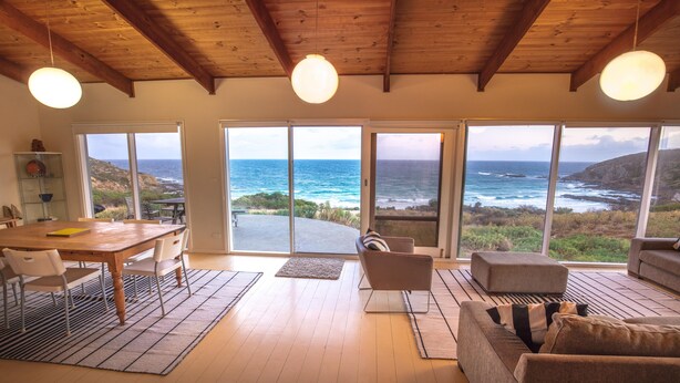 A spacious living area with a wooden ceiling, large windows offering ocean views, a dining table, and comfortable seating. - King George Beach Retreat (Middle River)