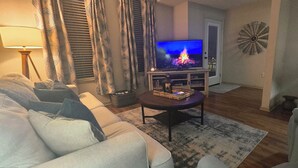 A living room with a sofa, a coffee table, a TV, and a lamp. - Downtown Loft: King/Queen Suites- 2½ Baths  Near Convention Center EV charging (Fort Smith)