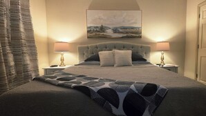 A neatly made bed with a patterned bedspread, two bedside lamps, a headboard, and a painting above the bed. - Downtown Loft: King/Queen Suites- 2½ Baths  Near Convention Center EV charging (Fort Smith)