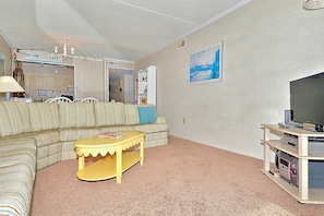Ein Wohnzimmer mit einem gestreiften Sofa, einem gelben Couchtisch, einem Fernseher auf einem Holzboden und einem Gemälde an der Wand.