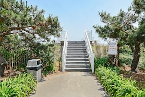 Eine Treppe führt zu einem privaten Eingang, umgeben von Pflanzen und bewölktem Himmel.