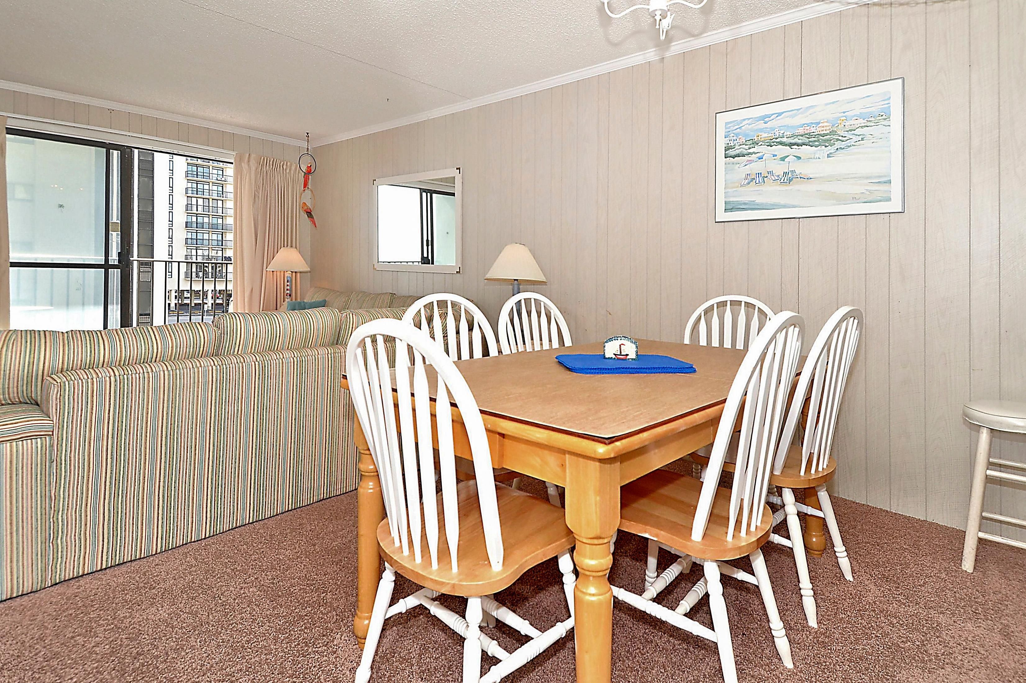 Une chambre d’hôtel comprenant une table à manger, des chaises, un canapé, une fenêtre avec des rideaux, un miroir et un tableau au mur.