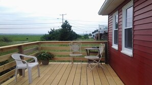 A wooden deck with two metal chairs and a small table, overlooking a green field.