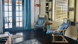 Una habitación acogedora con techo de madera, un ventanal con persianas y dos mecedoras con cojines estampados, además de una pequeña mesa.