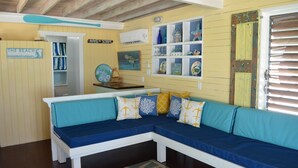 Una habitación con un banco azul y blanco, una estantería con adornos, y una puerta de aspecto rústico.