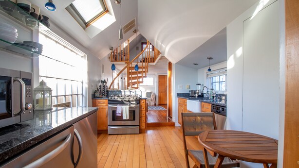 A modern kitchen with wooden floors, stainless steel appliances, and a wooden dining table.
