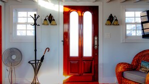 A room with a red door, a fan, a wicker chair, and two wall-mounted lamps.
