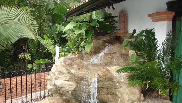 Ein Felswasserfall in einem Poolbereich mit umliegendem Grün und einer Backsteinmauer.