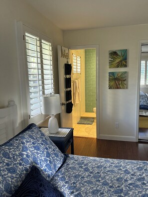 A bedroom with a bed, a nightstand, a lamp, and a view of a bathroom with a green wall and a towel rack.