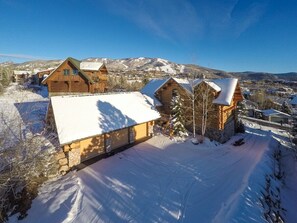 A log cabin with a snow-covered roof, surrounded by a snowy landscape and mountains in the background. - *Rare Find* Mark Twain Lodge by MVL - Luxury Cabin with Hot Tub - EZ Cancel (Steamboat Springs)