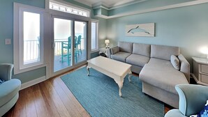 A living room with a large sliding glass door leading to a balcony, a grey sofa, a white coffee table, and a blue rug.