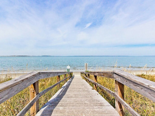 A wooden boardwalk leading to a beach with a calm sea and clear sky.