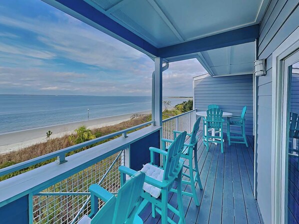 A covered deck with turquoise chairs and a view of the beach and ocean.