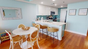 A modern kitchen with white cabinets, a central island, and a dining area with wicker chairs.