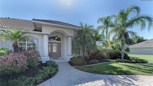 A two-story house with a tiled roof, a front porch, and a well-maintained garden with palm trees and shrubs.