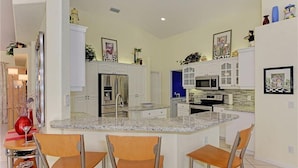 A modern kitchen with white cabinets, a central island, and bar-style seating.