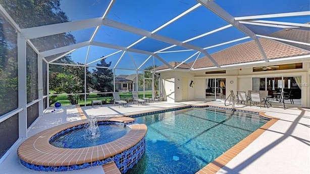 A swimming pool with a hot tub, surrounded by a covered patio area with lounge chairs.