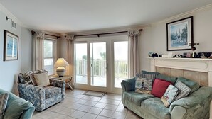 Un salon avec deux canapés, une table avec une lampe, une cheminée et un balcon avec des rideaux.