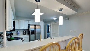 Une cuisine moderne avec des meubles blancs, un réfrigérateur en acier inoxydable, des chaises en bois et des luminaires suspendus.