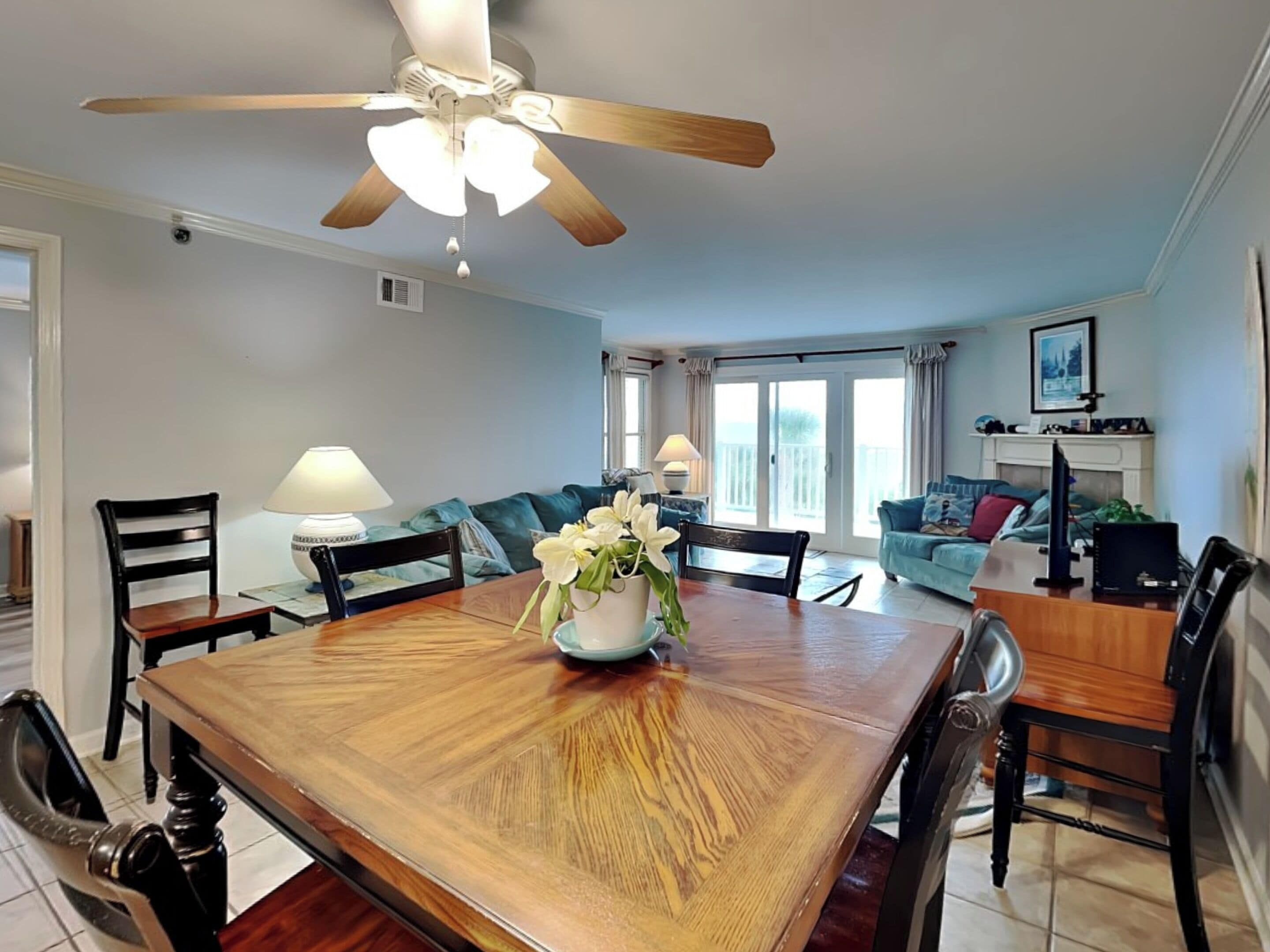 A dining area with a wooden table, chairs, a ceiling fan, and a vase with flowers.