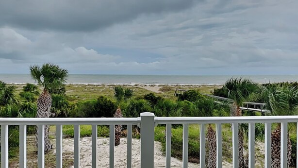 Une vue sur la plage, avec une balustrade blanche, des palmiers et un ciel nuageux.
