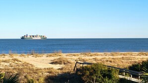 Un paysage côtier avec une plage de sable, une végétation clairsemée et une clôture en bois.