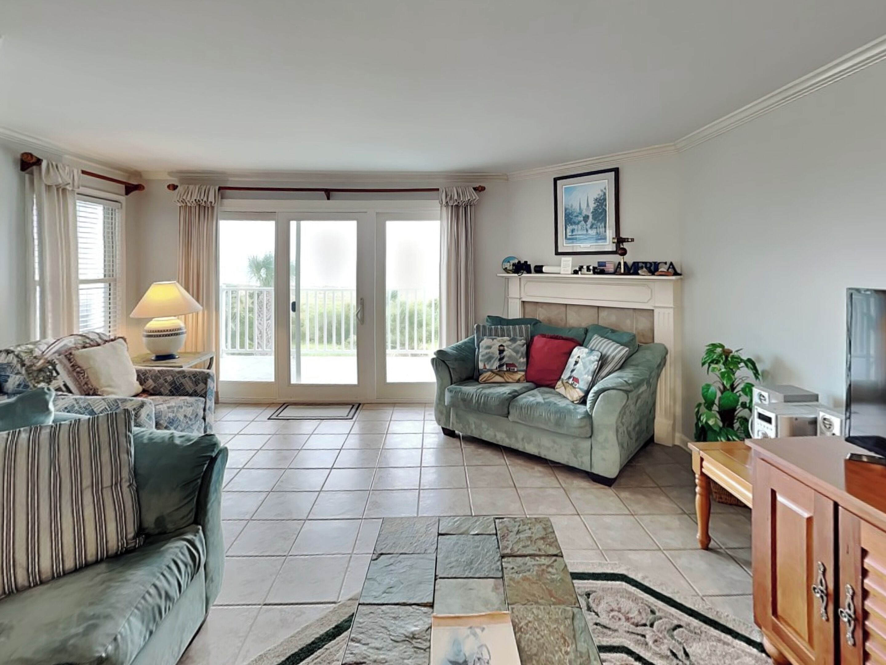 A living room with two sofas, a fireplace, a television, and a balcony with curtains.